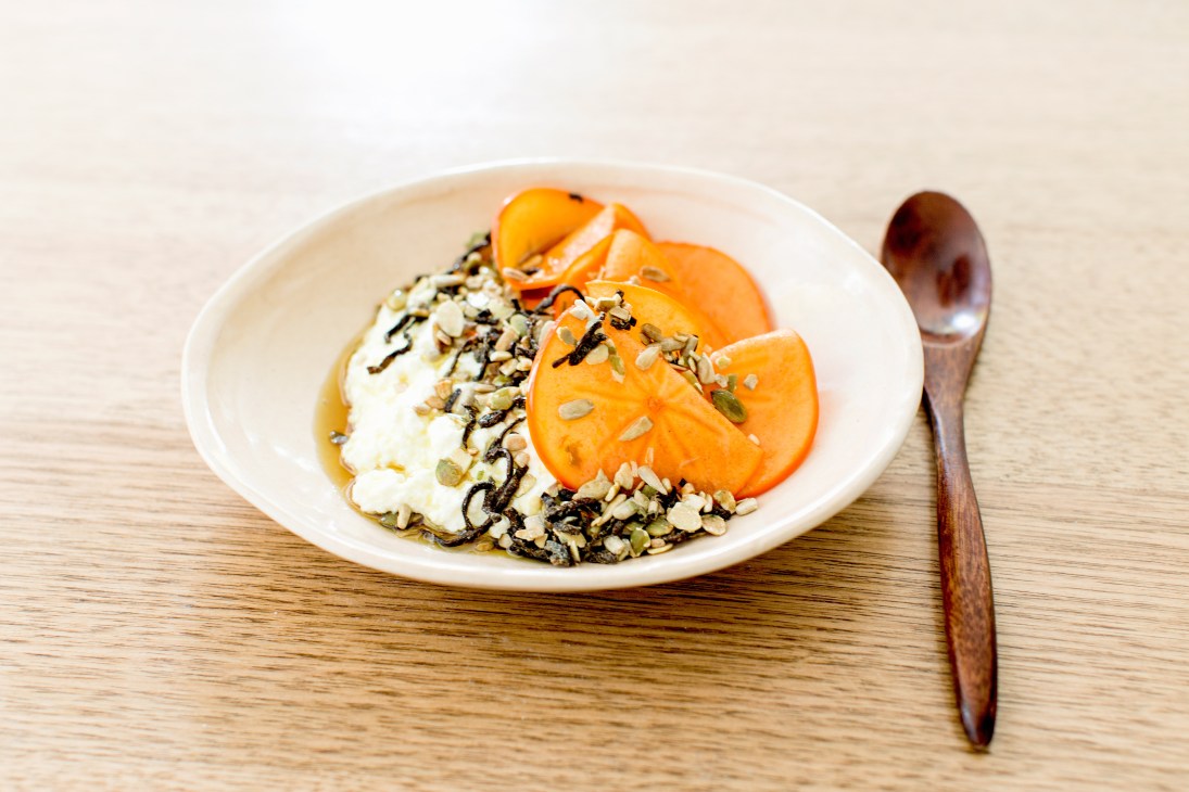 Ricotta and persimmon dish with furikake seasoning on a white plate with wooden spoon.