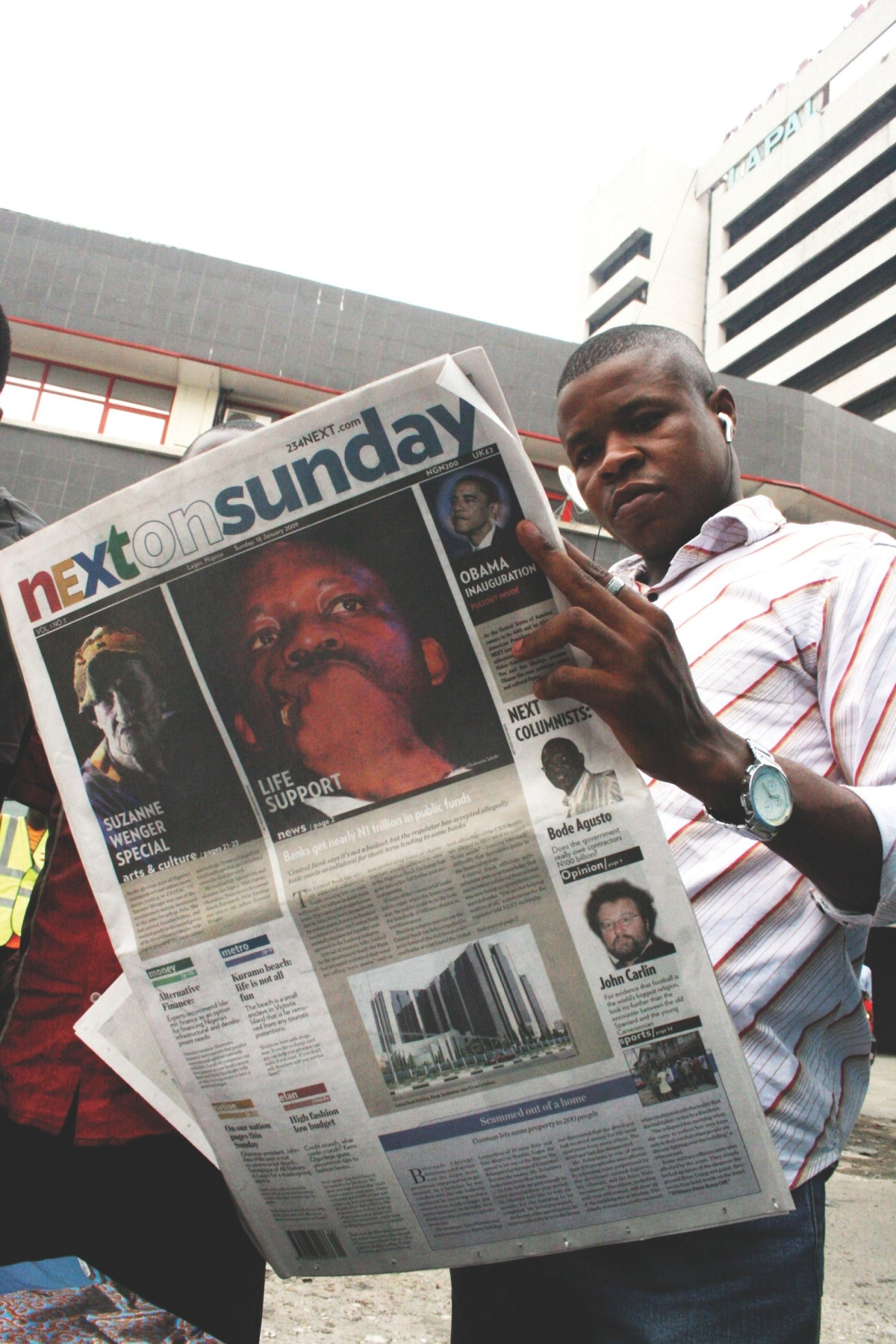 Man holding open NEXT newspaper showing front page with Obama inauguration coverage in Lagos.