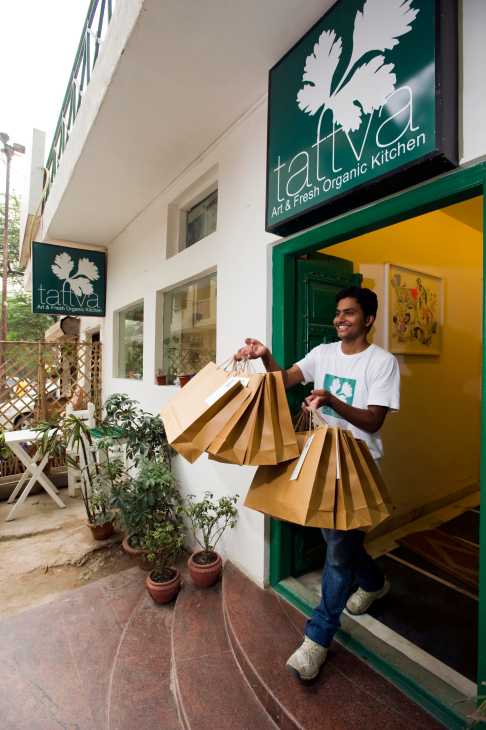 Man holding multiple brown paper delivery bags outside Tattva Art & Fresh Organic Kitchen in New Delhi