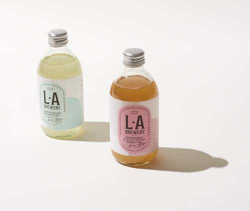 Two bottles of LA Brewery kombucha with pale yellow and amber-colored drinks in glass bottles with metal caps.