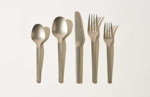 Five stainless steel utensils arranged in a row: two spoons, a knife, and two forks by Heath Ceramics.