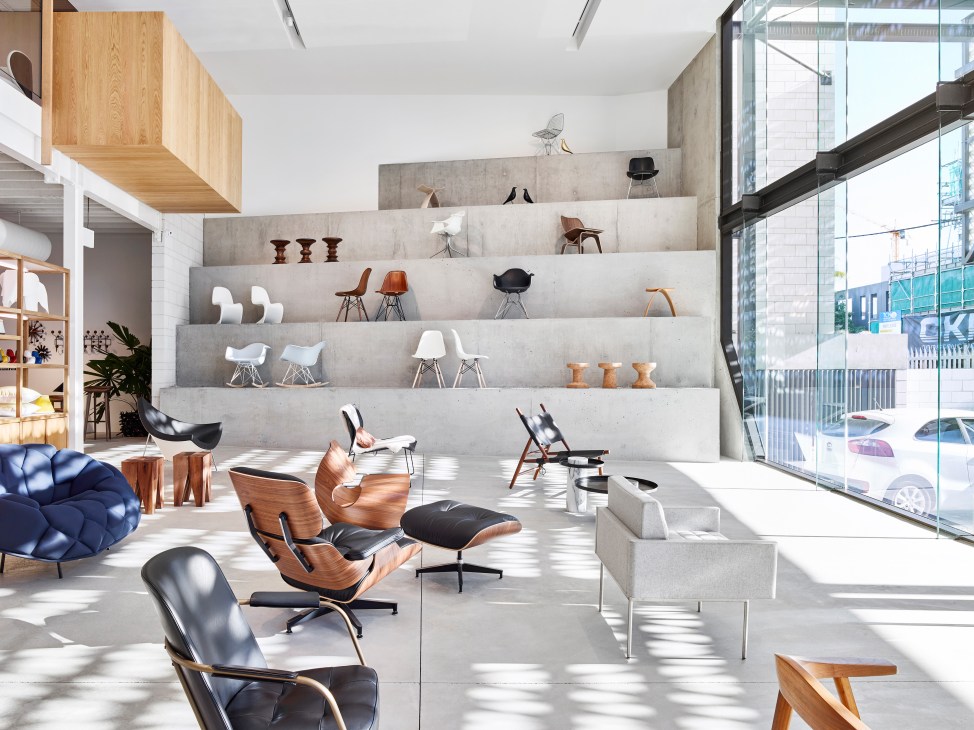 Modern furniture showroom with tiered concrete display shelves showcasing designer chairs and stools
