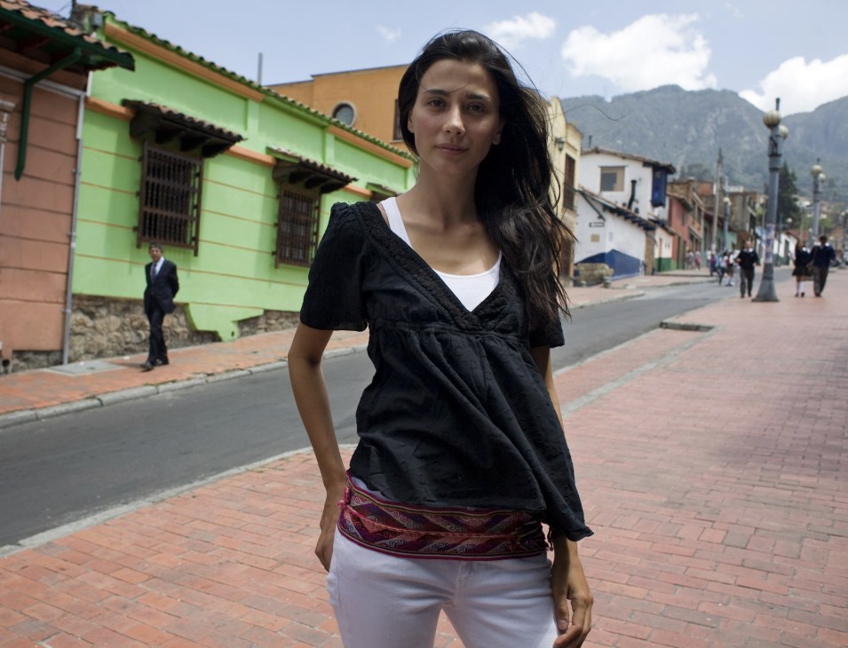 Woman standing on a brick street in La Candelaria with colorful colonial buildings and Andean mountains in the background.
