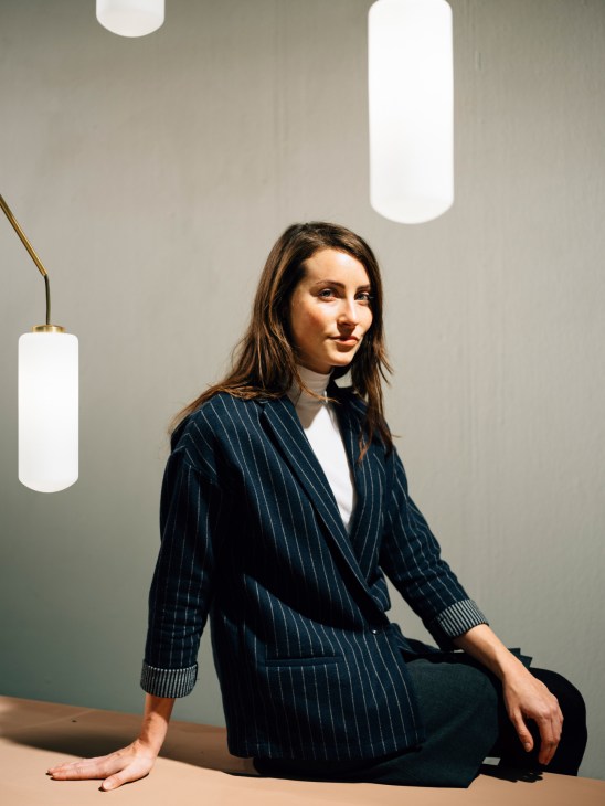 Cassandra Bradfield, head designer at Frama, sits at a table surrounded by cylindrical pendant lights.