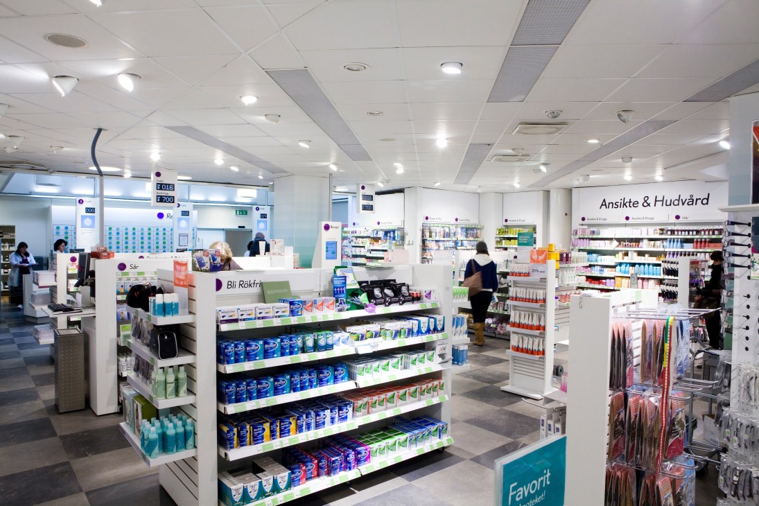 Interior of Apoteket pharmacy showing white ceiling, shelving with products, and service counter with staff.