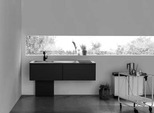 Minimalist black kitchen sink and cabinet unit with large window overlooking trees.