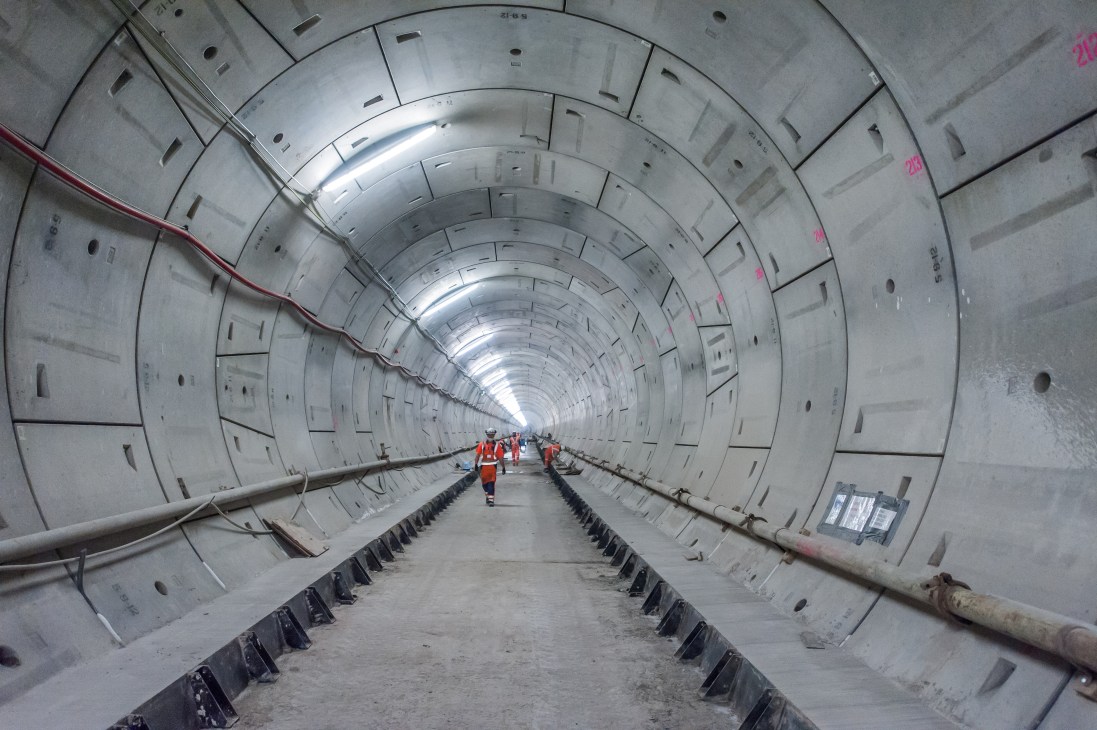 Interior of a large tunnel under construction with workers in safety vests walking through.