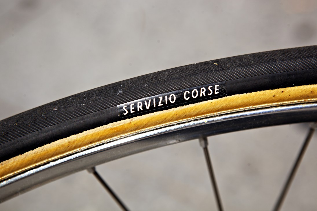 Close-up of a Servizio Corse bicycle tire with tan-colored sidewall and chrome rim detail.