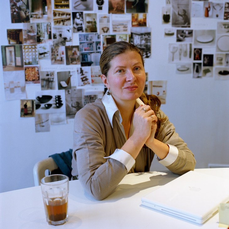Woman at desk with inspiration board of photos and design materials behind her at Studioilse design studio.