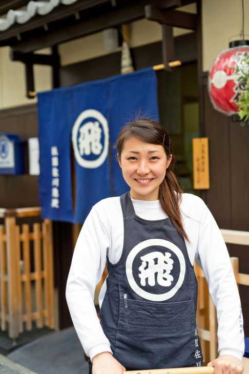 Staff member at Gion Sagawa Kyubin delivery service in Kyoto wearing branded apron outside traditional wooden machiya house.