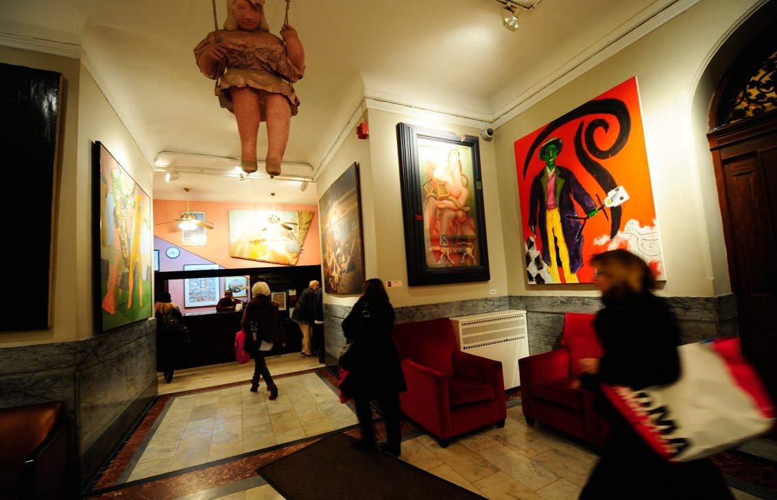 Interior of Kronenhalle restaurant in Zürich showing diners, colorful modern artworks on walls, and red chairs.