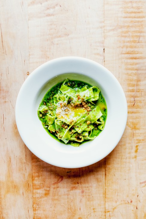 Fettuccine with green kale pesto, grana padano cheese and garnish in a white bowl on a wooden surface.
