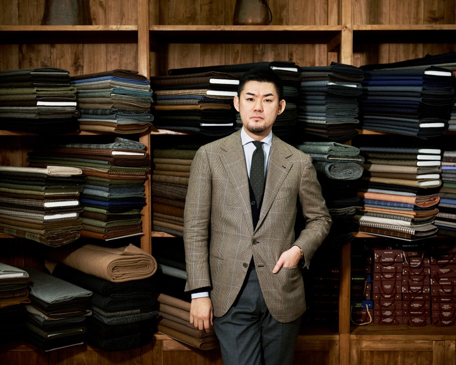 Kotaro Miyahira, a Japanese tailor, stands in front of shelves of fabric swatches at his Florence tailoring shop.