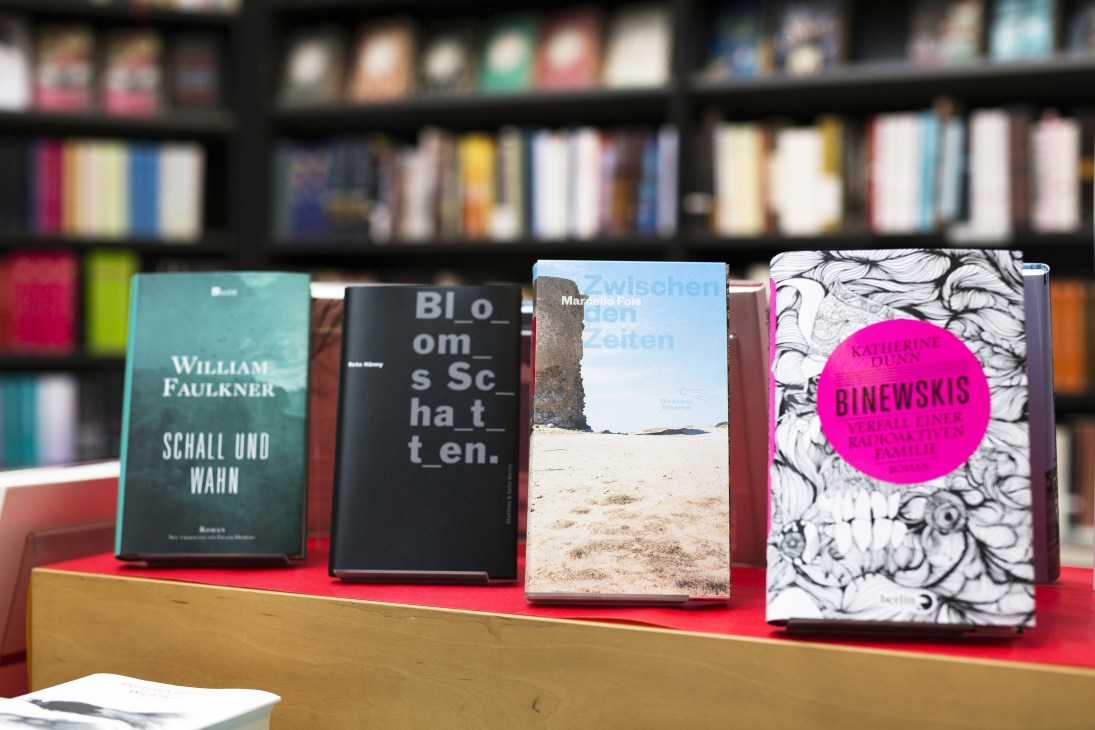 Books displayed on a red shelf in front of bookshelves at Osiander bookstore in Tübingen, Germany.