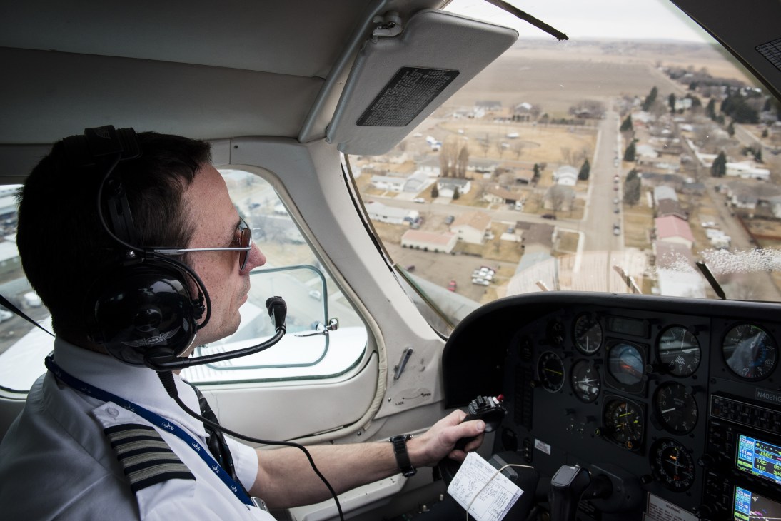 Pilot Sam Lyman at the controls of a small Cessna aircraft flying over Montana landscape.
