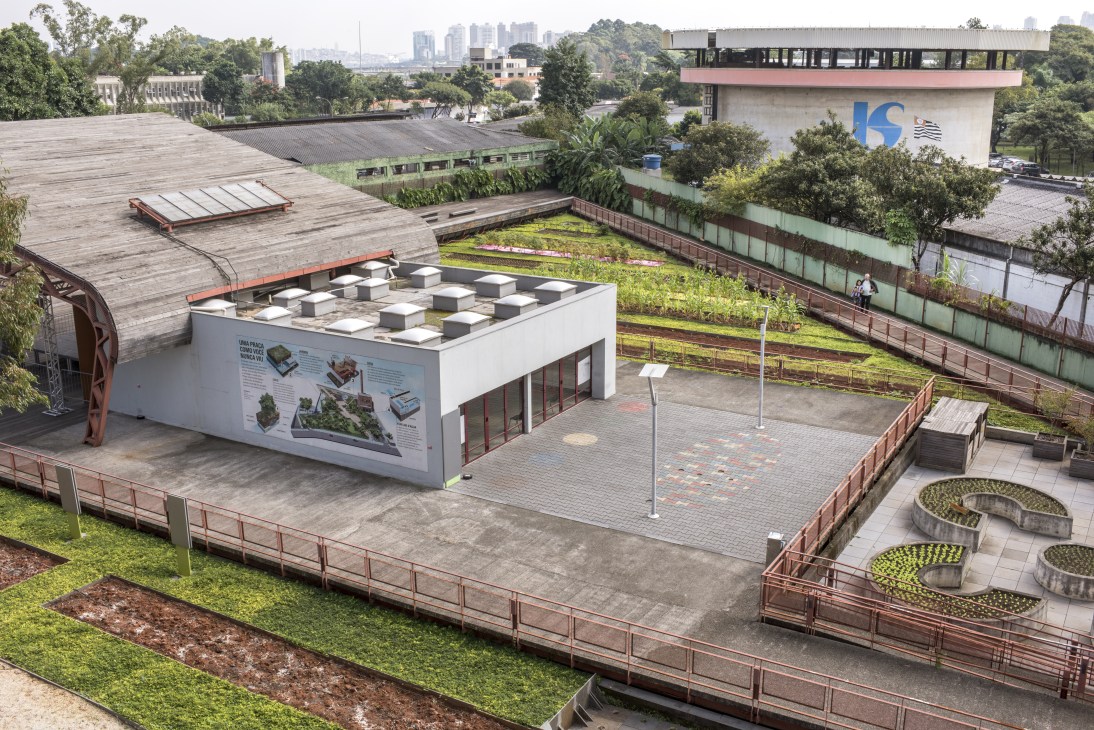 Aerial view of Victor Civita Square in São Paulo showing raised wooden walkway, planted beds, and green space with city skyline in background.