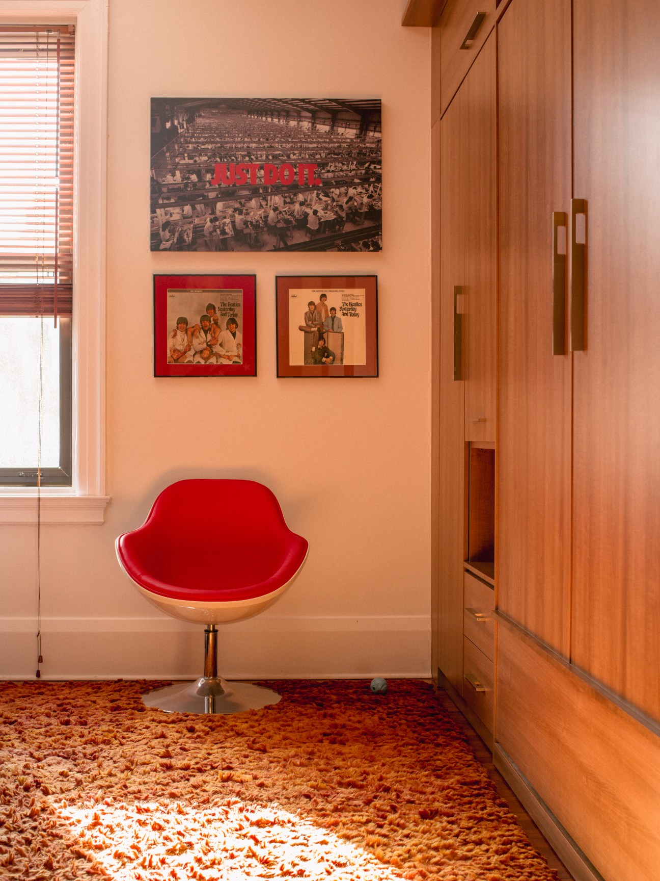 Red mid-century modern chair with wooden base against peach wall displaying Beatles album covers and vintage photographs.