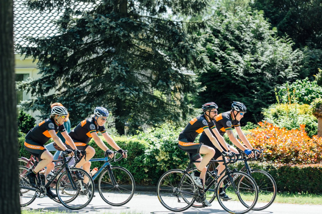 Four cyclists in orange and black team jerseys riding on a tree-lined path in Utrecht.