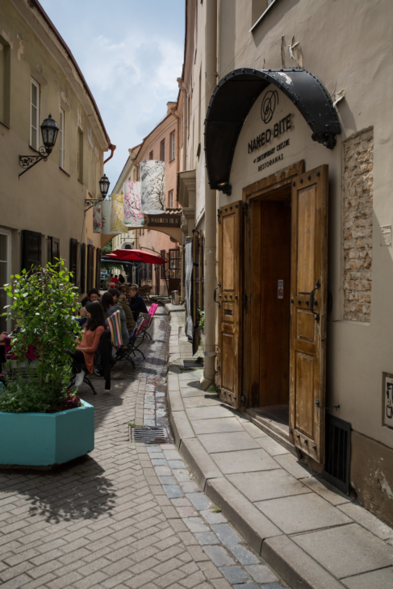 Narrow cobblestone street in Vilnius old town with Naked Bite restaurant entrance and historic buildings.