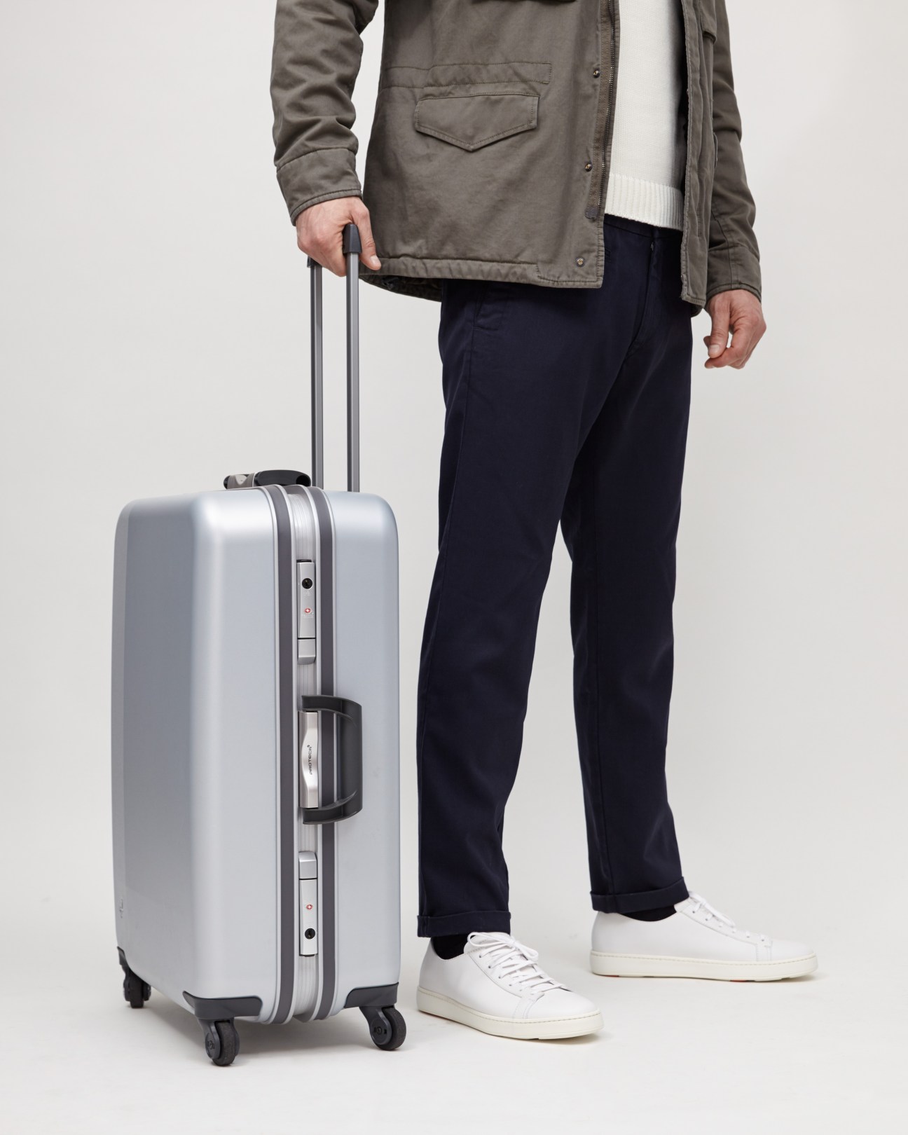 Man holding silver Proteca luggage with impact-resistant resin shell and magnesium-alloy frame.