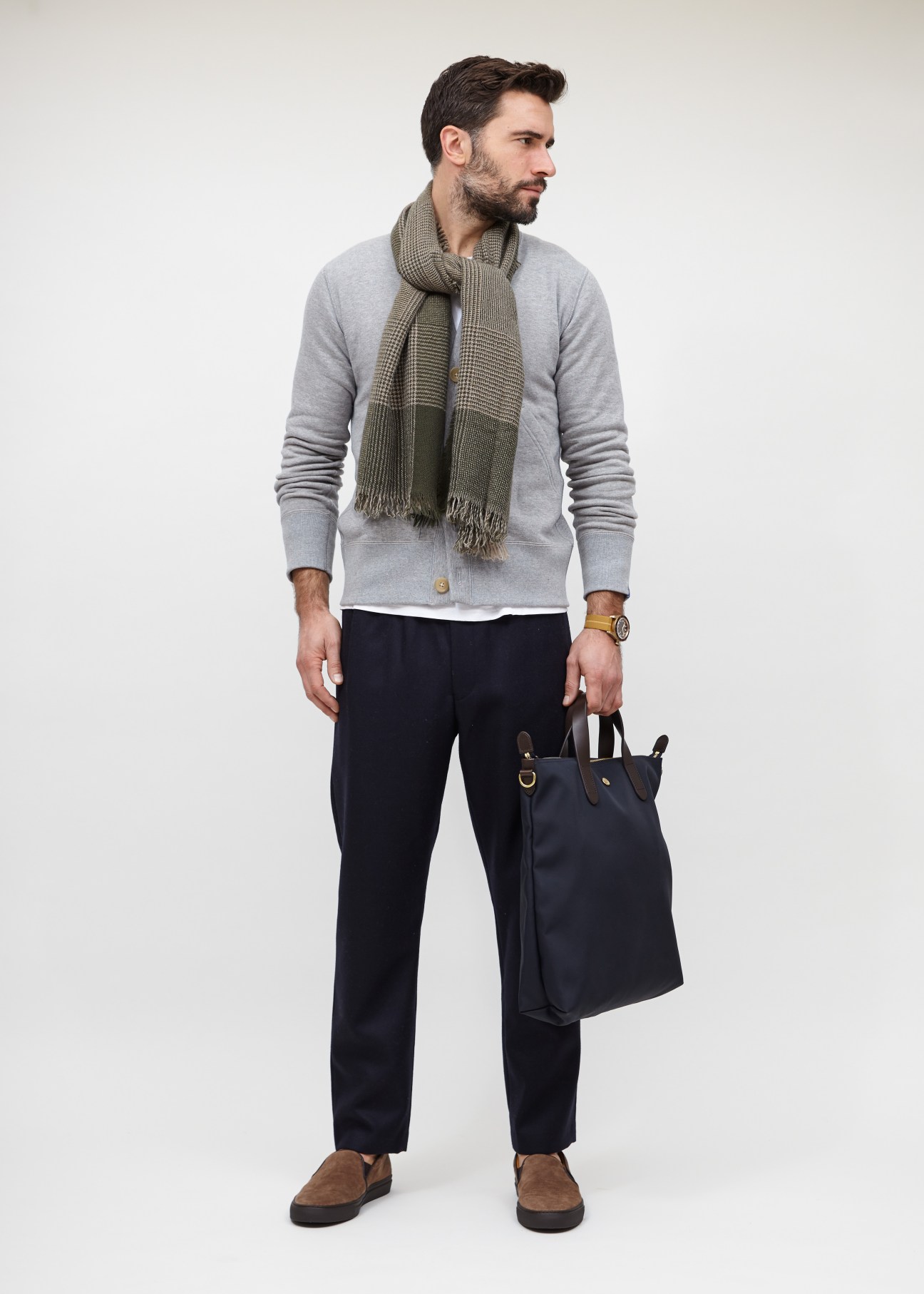 Man wearing casual layered travel outfit with cardigan, scarf, and navy bag