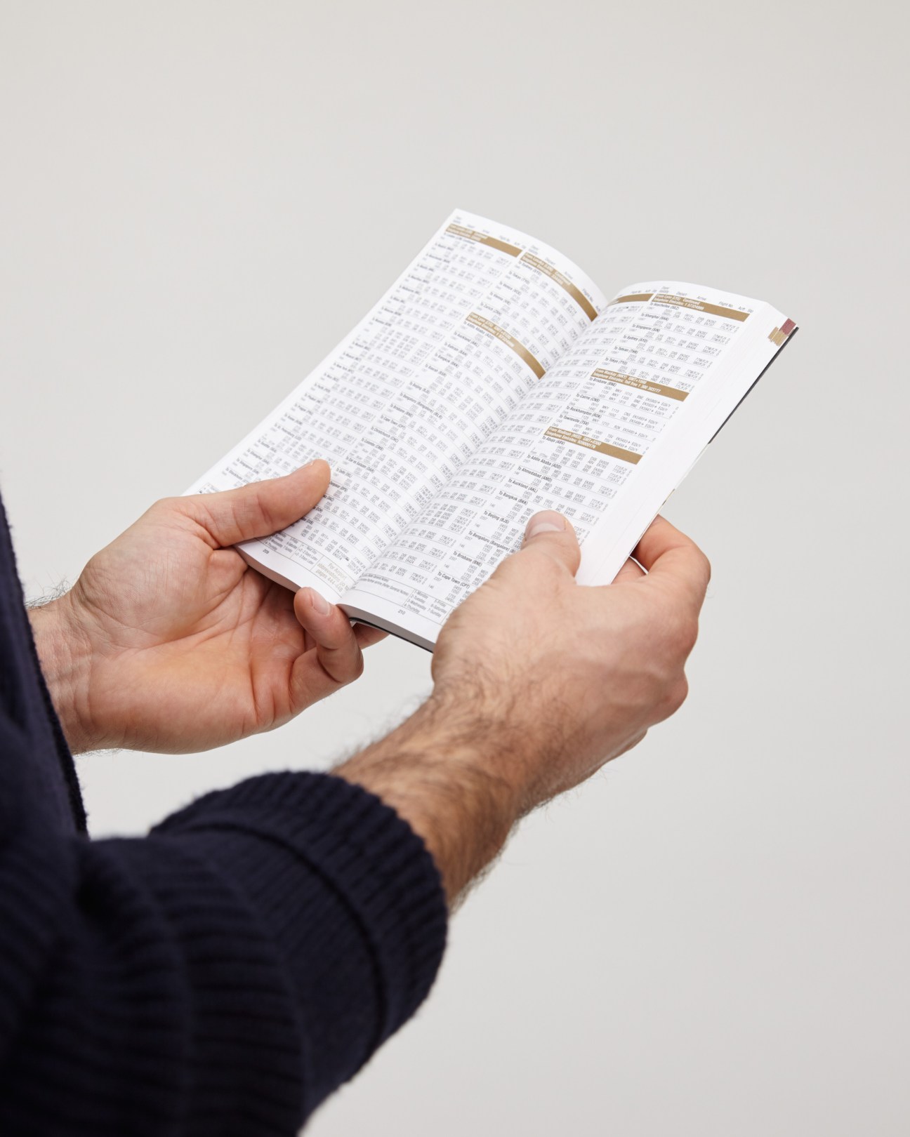 Hands holding an open Emirates printed flight timetable with flight schedules and route information.