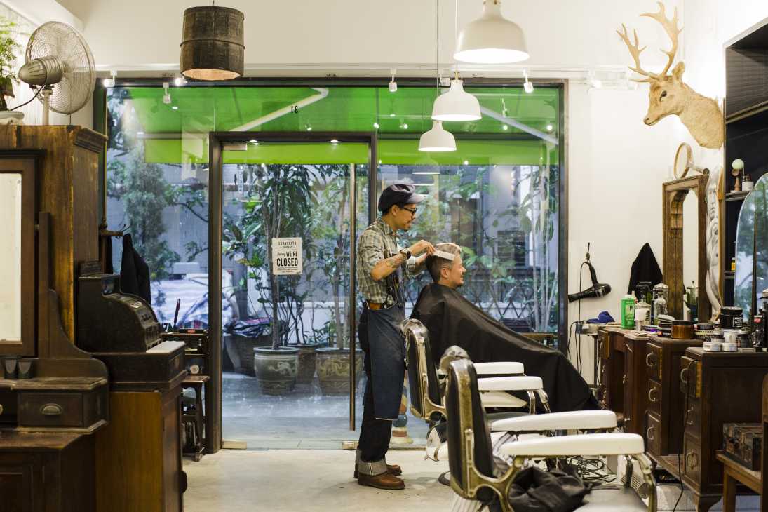 A barber cuts a customer's hair inside Hair House Barbershop in Hong Kong, surrounded by vintage furniture and decor.
