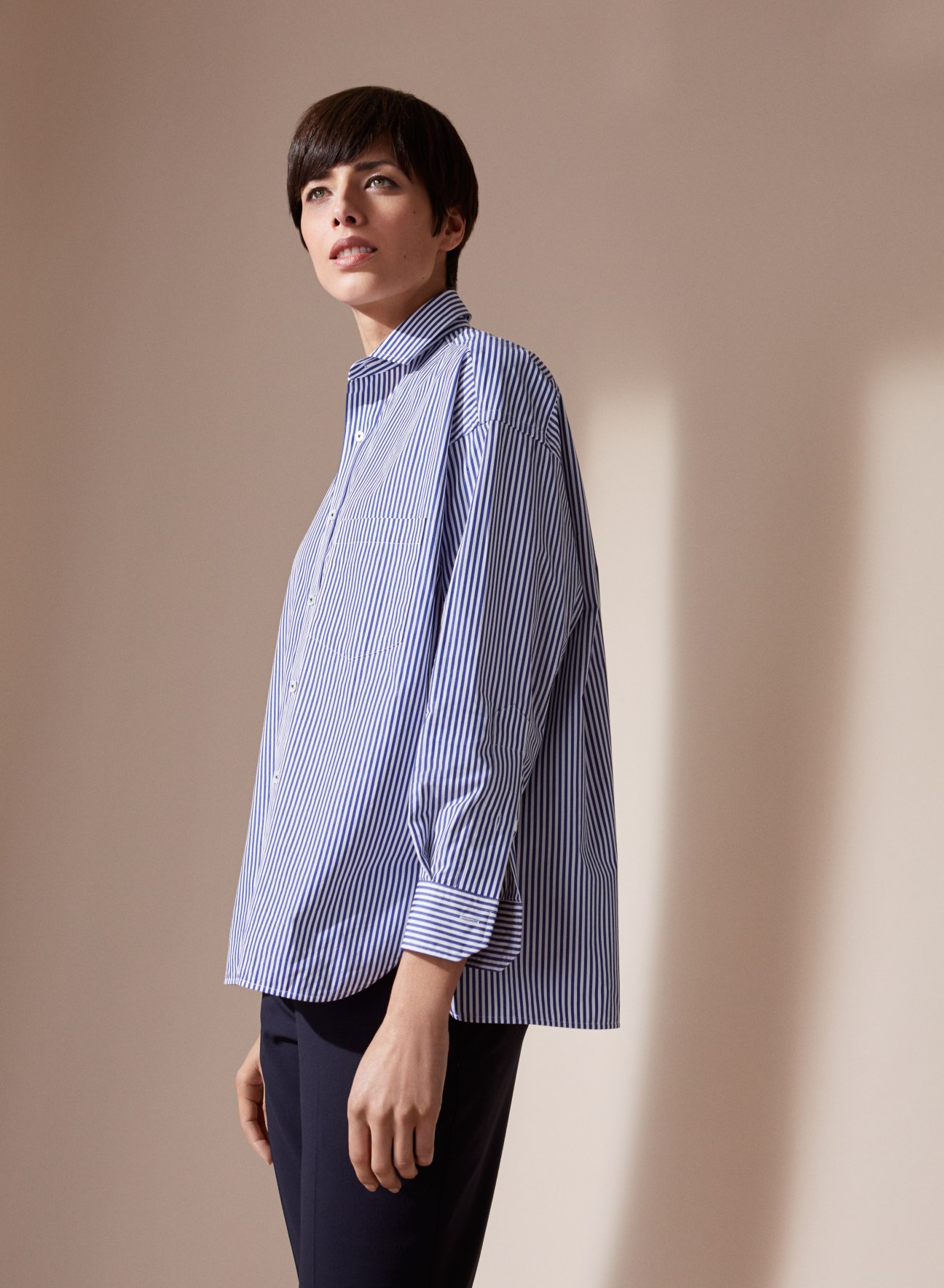 Woman wearing an oversized blue and white striped Oxford shirt.