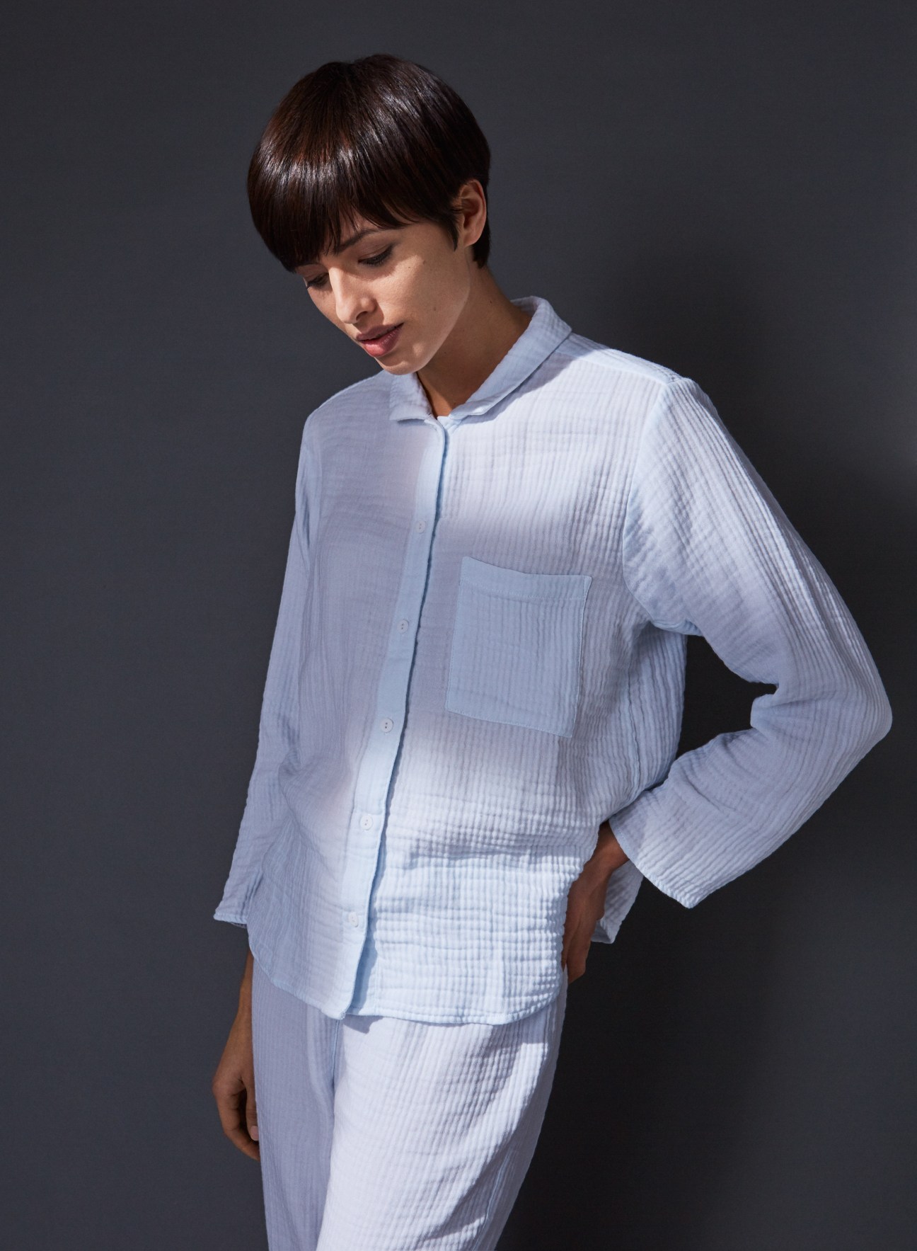 Woman wearing light blue pajama shirt and matching pants against gray background