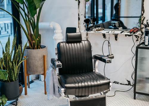 Interior of Blind Barber barbershop with black leather barber chair and potted plant.