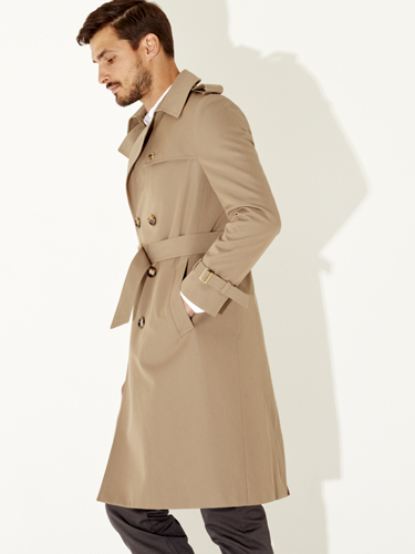 Man wearing a beige trench coat over dark trousers, photographed in profile against a white background.