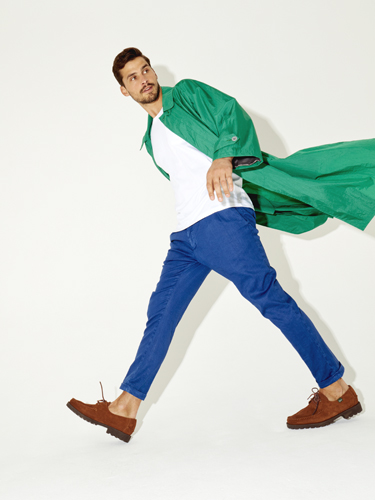 Man wearing green jacket, white shirt, blue trousers and brown suede boots jumping dynamically.