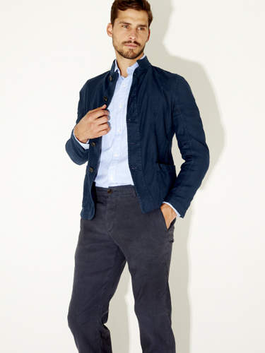 Man wearing navy quilted jacket, light blue shirt, and dark trousers against white background.