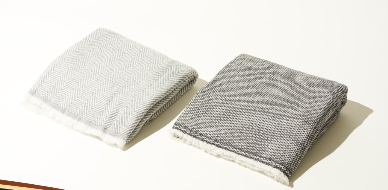 Two folded cashmere throws in cream and grey with herringbone weave patterns by Slate + Salt.