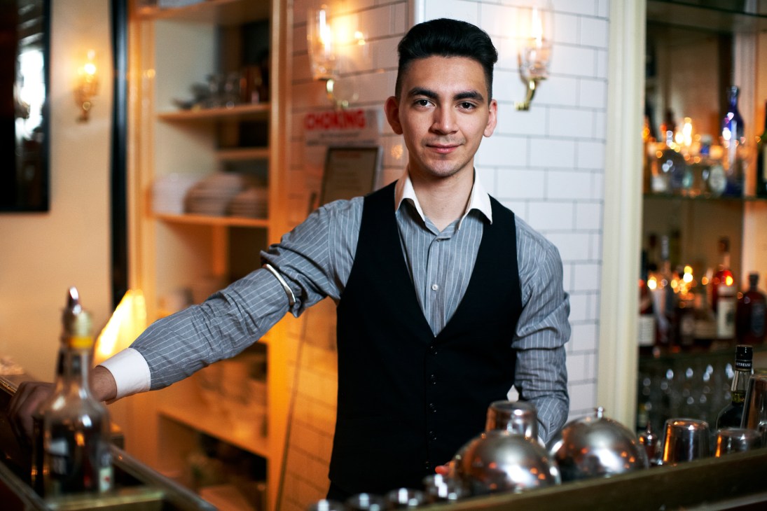 Bartender Danny Gil at Weather Up bar in New York, pouring a drink behind the copper-topped bar.