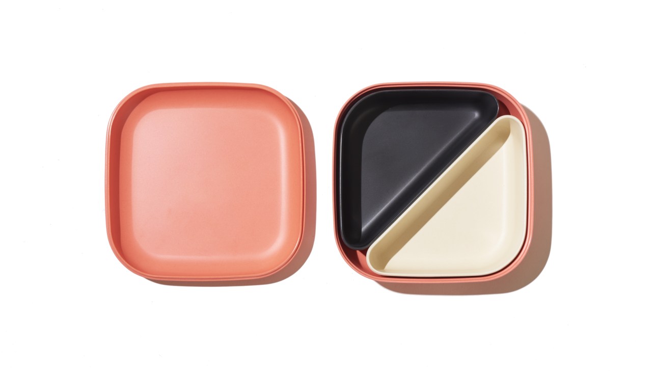 Two coral-coloured bamboo-fibre bento boxes by Ekobo, one empty and one containing black and cream compartments.