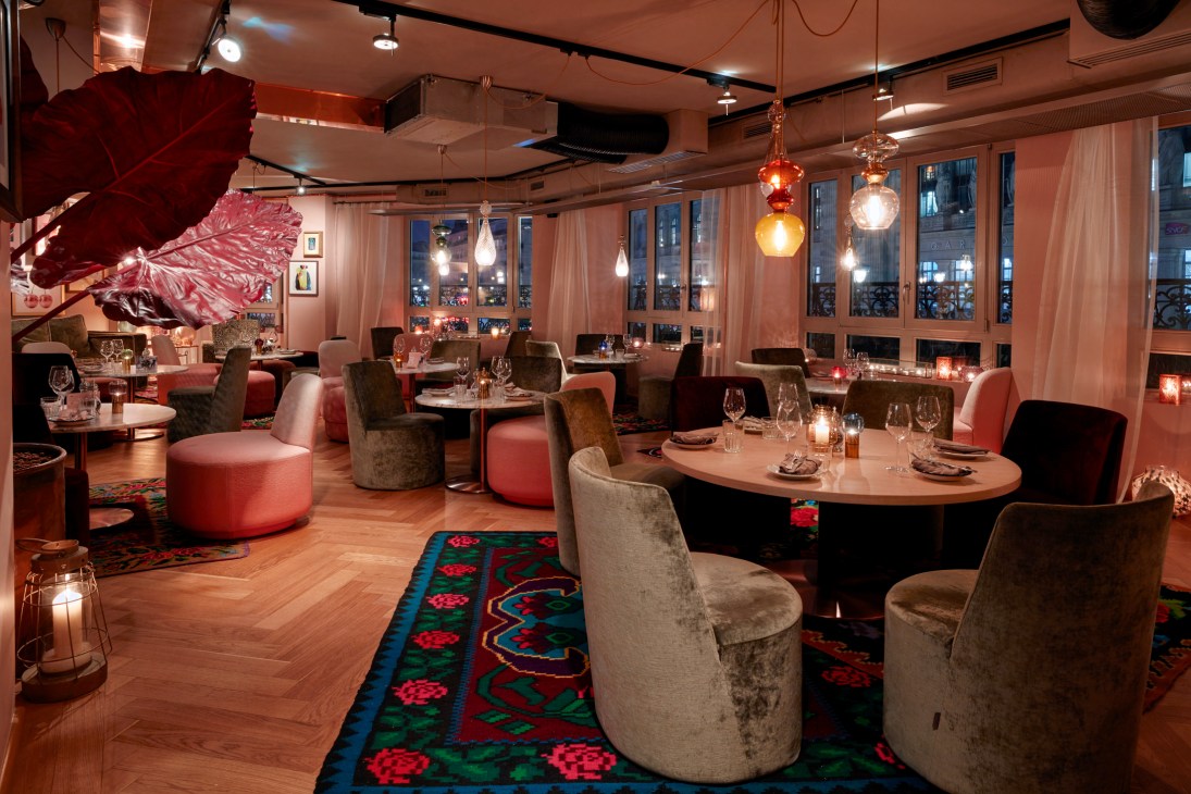 Modern restaurant interior with colorful pendant lights, pink velvet chairs, and patterned carpets at Neni restaurant in 25hours Hotel Terminus Nord Paris.