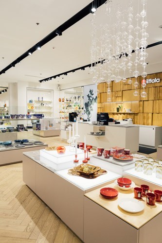 Interior of Iittala shop in Helsinki with modern display tables showcasing red ceramics and glassware.