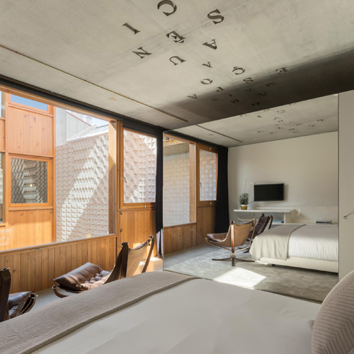 Modern hotel bedroom with exposed concrete ceiling, large windows, wooden paneling, and twin beds