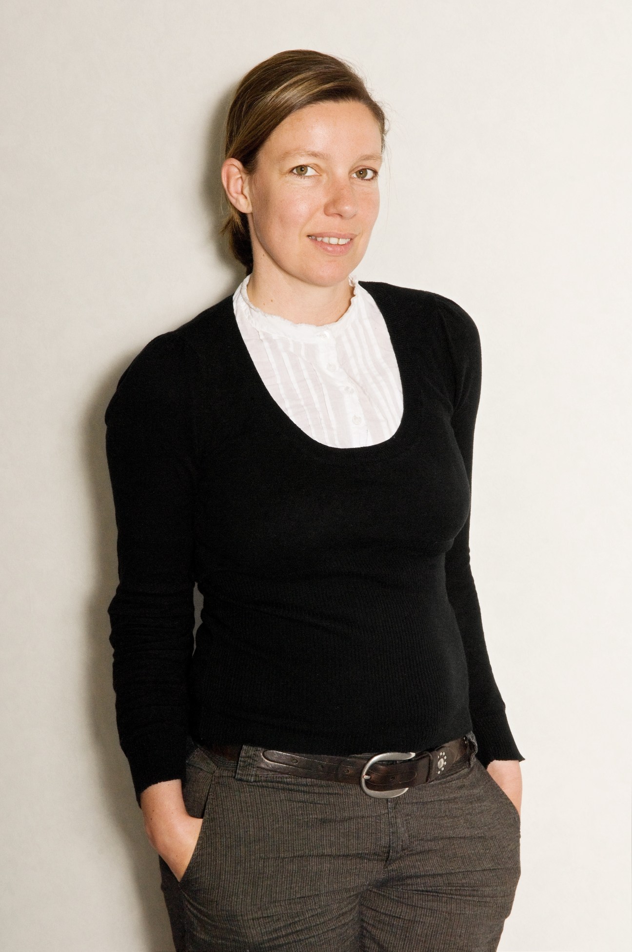 Portrait of a woman in a black sweater and white collared shirt against a white wall.
