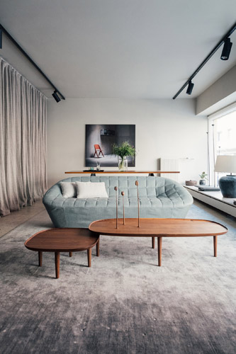 Interior of Poiat design studio showing minimalist furniture including a curved gray sofa and wooden coffee table.
