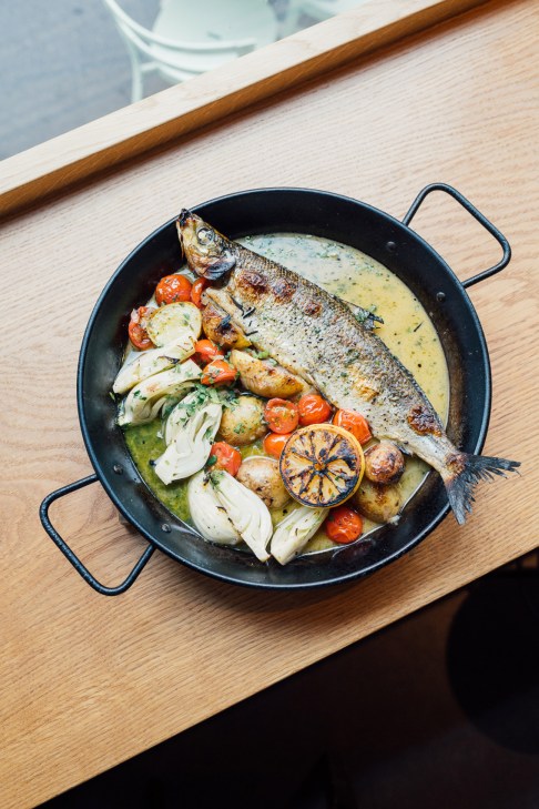Whole roasted fish with vegetables and lemon in a black pan at Pontus restaurant in Helsinki.