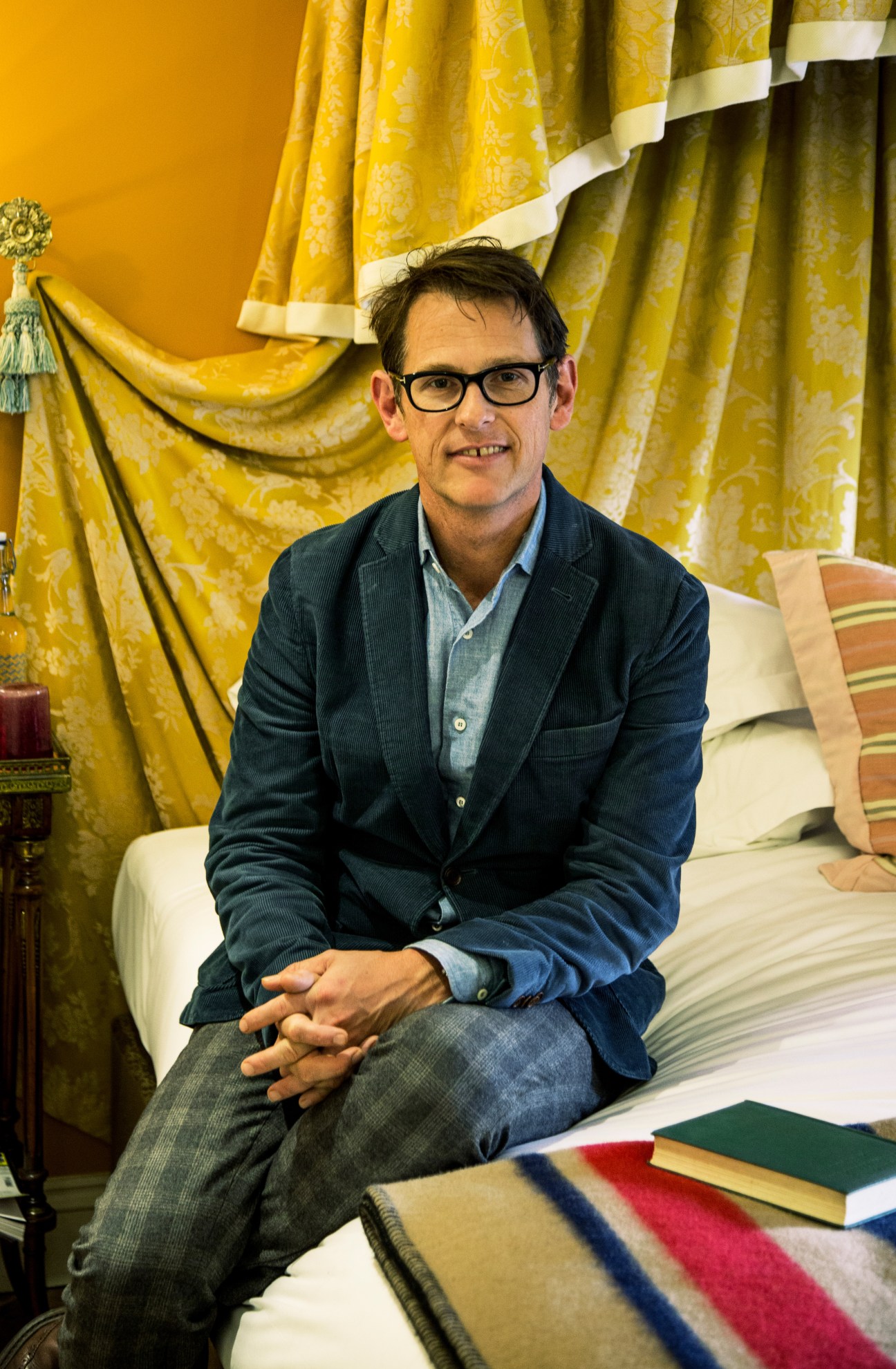 Man sitting on bed in hotel room with yellow patterned curtains behind him