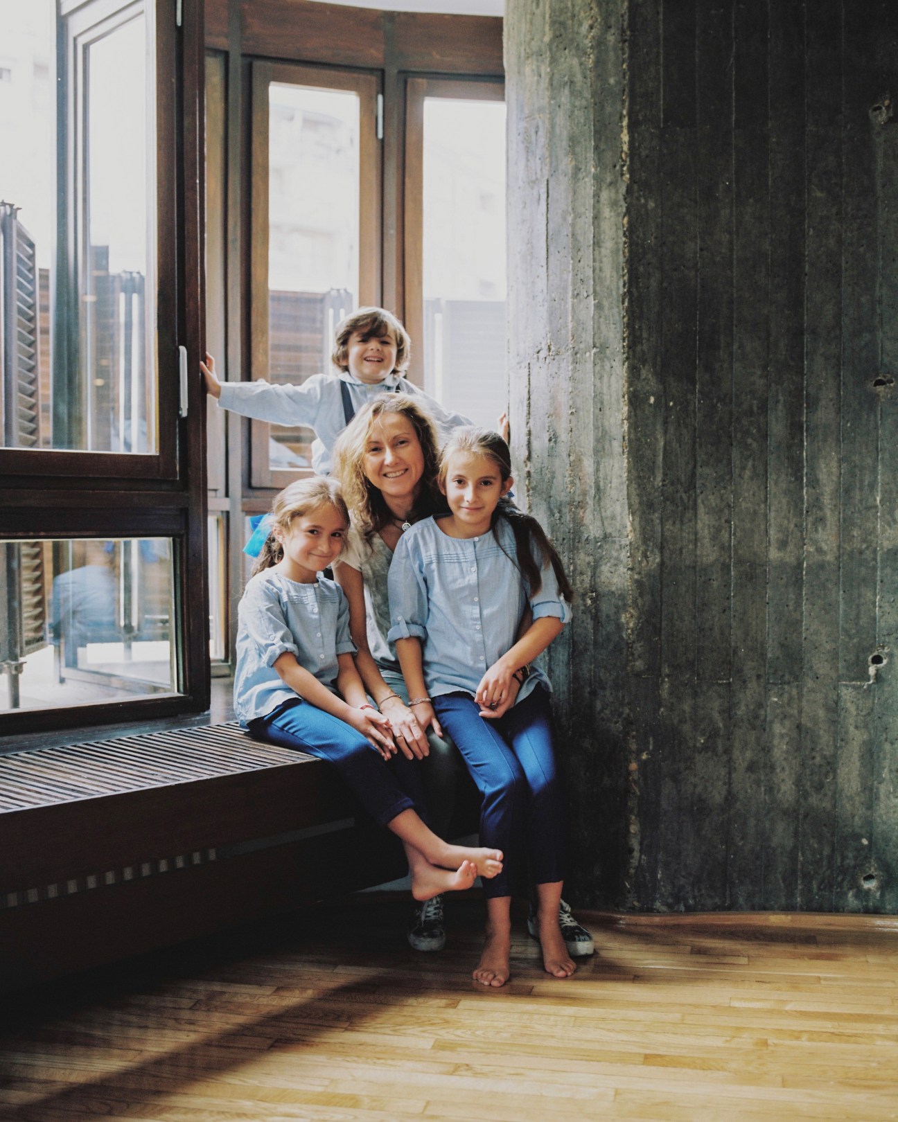 Woman and three children sitting on a window sill in Torres Blancas, Madrid, with city skyline visible through large windows behind them.