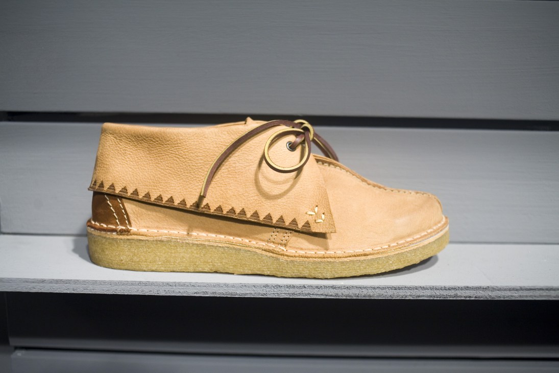 Tan leather desert boot with crepe sole and decorative stitching on display shelf.