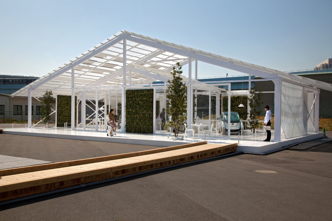 Modern white modular building with steel frame structure, glass panels, vegetation walls, and people inside and outside.