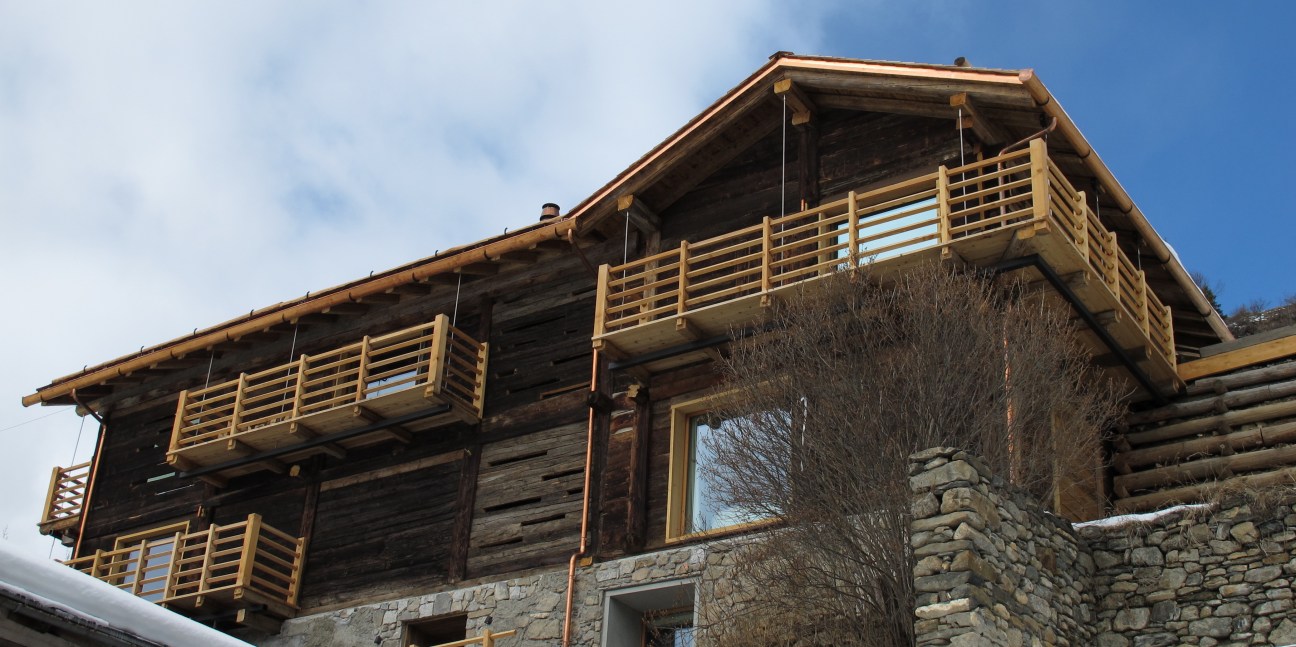 A rustic wooden barn with stone foundation and wooden balconies in Commeire, Switzerland.
