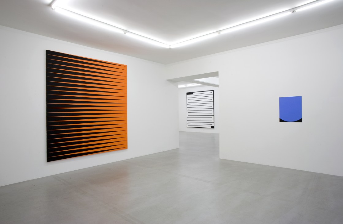 Gallery Nordenhake's minimalist Stockholm space with white walls, geometric artworks including orange and black striped canvas and blue abstract piece.