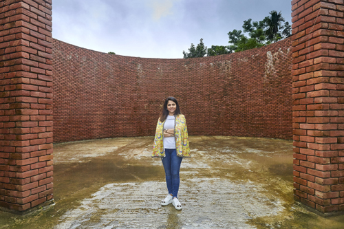 Person standing in an empty brick courtyard surrounded by tall red brick walls.