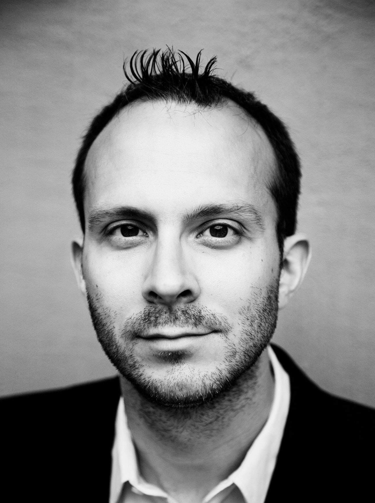Black and white portrait photograph of a man with dark hair and beard wearing a dark jacket and white shirt.